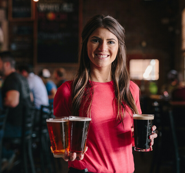 Fröhliche Kellnerin, die ihren Gästen Bier bringt